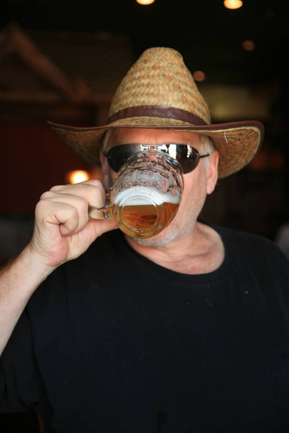 Piwo. Mężczyzna pijący piwo. Faceta pijącego kubek piwa. Szczęśliwy elegancki człowiek pijący piwo. Facet pijący piwo z kubka piwa. Człowiek ze szklanką piwa. Mężczyzna trzyma szklankę piwa. Facet pijący piwo w pubie. Browar. Hipster pije piwo. Wszystkiego najlepszego. - Zdjęcie, obraz
