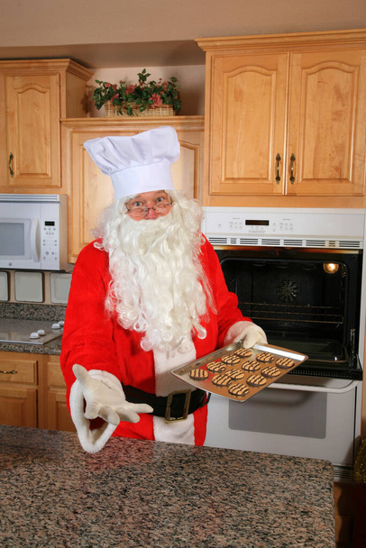 Joulupukki leipoo keksejä. Joulukeksejä. Joulupukin nähdään leipovan joulukeksejä uuninsa sisältä. Tuoreita keksejä. Joulupukki leipoo jouluksi. Talvilomaevästeet. Uunissa leipomassa keksejä. On Cookien aika. Ho Ho Ho - Valokuva, kuva