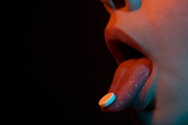 Close-up of pill on woman tongue. Tongue holds pills in open mouth. Close up of ill sick woman taking pill to relieve pain concept, daily supplements or antibiotic antidepressant into mouth. - 写真・画像