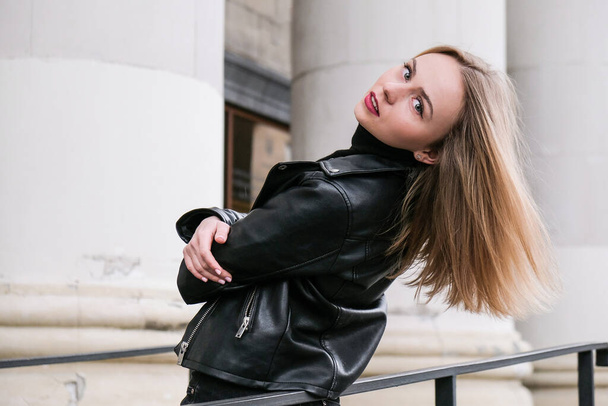 Portrait of young blonde woman with red lips wearing leather jacket on corporate building stairs. Career businesswoman. Urban street city lifestyle - Фото, зображення