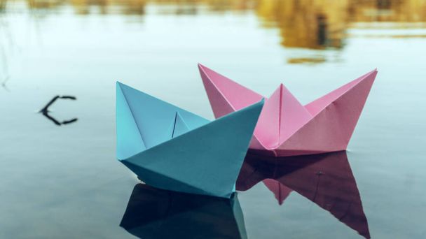 Twee papieren boten van rode en blauwe kleur, drijvend op het water. Zomer dag op de oever van de rivier. Spelen met papieren boten. 4K. - Foto, afbeelding