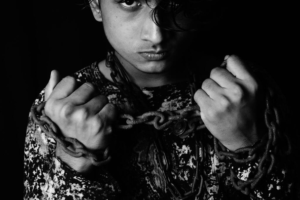 A grayscale portrait of an angry asian man with a metal chain around his neck and hands - Foto, Imagen