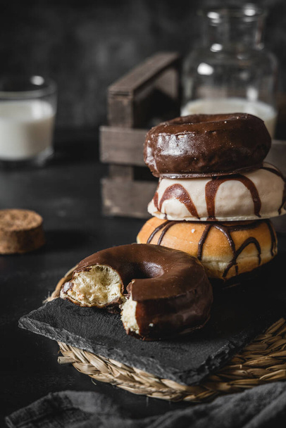 A vertical shot of a stack of donuts with chocolate and caramel frosting on a black decorated table - Фото, зображення