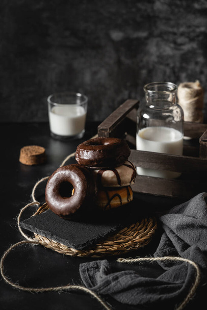 A vertical shot of a stack of donuts with chocolate and caramel frosting on a black decorated table - Foto, Imagen
