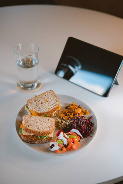 A vertical shot of a bowl of delicious vegan food with sandwiches and a glass of water in front of a tablet - Valokuva, kuva