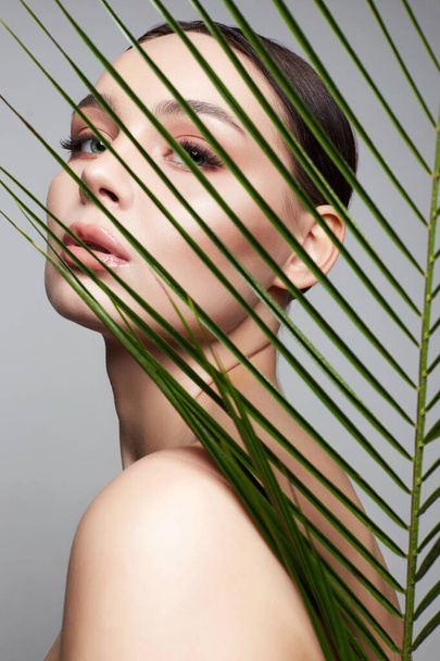beautiful girl in palm leaves. Beautiful young woman with Make-up. Beauty Portrait. Natural cosmetics - 写真・画像