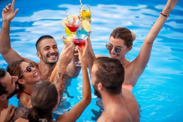 Gruppo di amici che fanno festa in piscina, bevono cocktail e si divertono insieme. - Foto, immagini