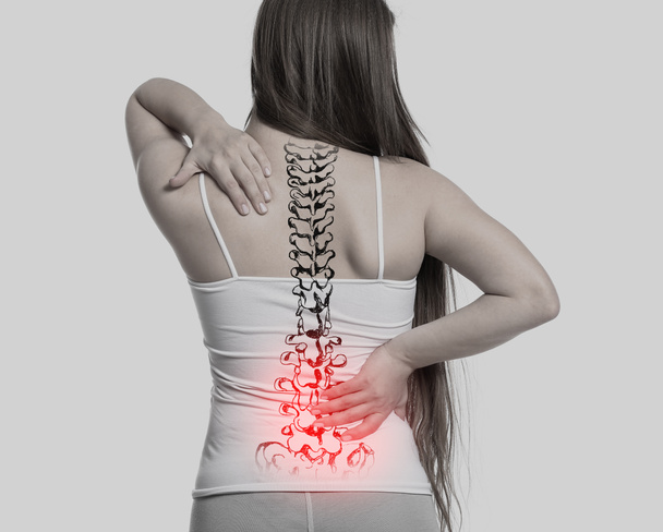 Νεαρή γυναίκα που υποφέρει από πόνο στην πλάτη σε ανοιχτό φόντο - Φωτογραφία, εικόνα