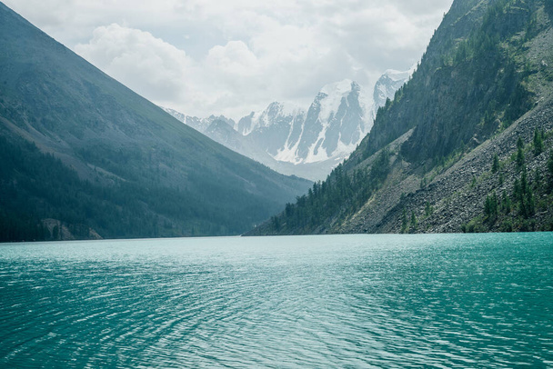 Καταπληκτική θέα στο διαλογιστικό κυματισμούς σε γαλάζιο καθαρά ήρεμα νερά της λίμνης βουνού στο φόντο χιονισμένα βουνά. Ατμοσφαιρικό τοπίο με αλπική λίμνη, δέντρα και παγετώνες. Χαλαρώστε τα κύματα στα γαλαζοπράσινα νερά. - Φωτογραφία, εικόνα