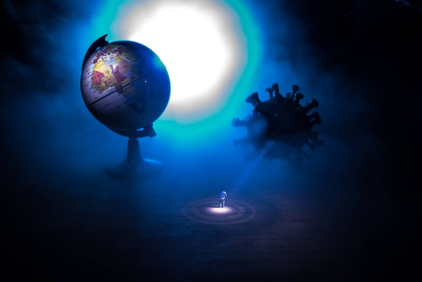Παγκόσμια ιδέα πανδημίας του ιού Κορόνα. Μινιατούρα άνθρωπος στέκεται κοντά στο μεγάλο μυθιστόρημα του ιού Κορόνα στο σκοτάδι. Δημιουργική διακόσμηση με ομίχλη και backlight. Επιλεκτική εστίαση - Φωτογραφία, εικόνα