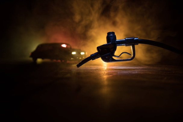 Creative concept. Silhouette of gasoline pistol miniature on dark toned foggy background. Close up. Car miniature on background. Selective focus - Foto, immagini