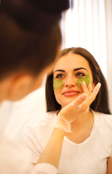 Професійний косметолог наносять зелені плями на неспокійну зону спокійної жінки, яка відвідує клініку краси
 - Фото, зображення