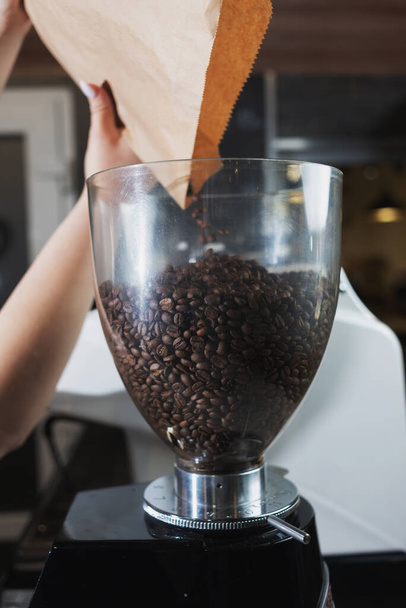 close-up of a baristas hand pouring coffee beans into the grinding tank of a coffee grinder. Professional machine for grinding coffee beans. - Fotografie, Obrázek