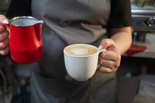 カフェやコーヒーショップでカプチーノと牛乳を手にした女性バーテンダーバリスタ。少女はコーヒーを飲んでいる。ラテだ。コーヒー製造技術の概念. - 写真・画像