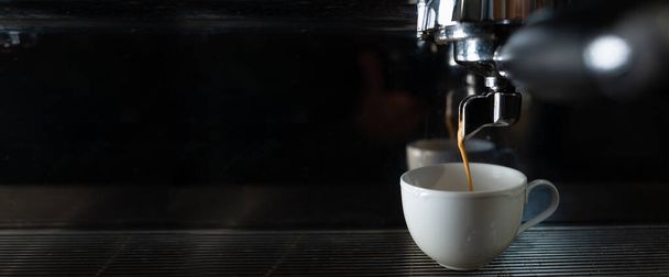 Kávovar a keramický bílý šálek kávy v kavárně. Reklamní plakát a příprava kávy. Profesionální kávové vybavení. - Fotografie, Obrázek