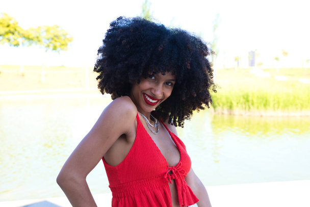 kaunis afro amerikkalainen nainen hymyilee ja katselee kameraa tekee erilaisia asentoja ja eleitä hänen kasvonsa. Naisella on punainen toppi ja punainen huulipuna. Käsite onnellisuus - Valokuva, kuva