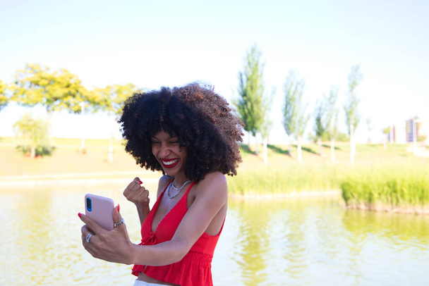 Bella donna afro-americana che parla in videochiamata è molto felice. La donna indossa un top rosso. Concetto di videochiamata. - Foto, immagini