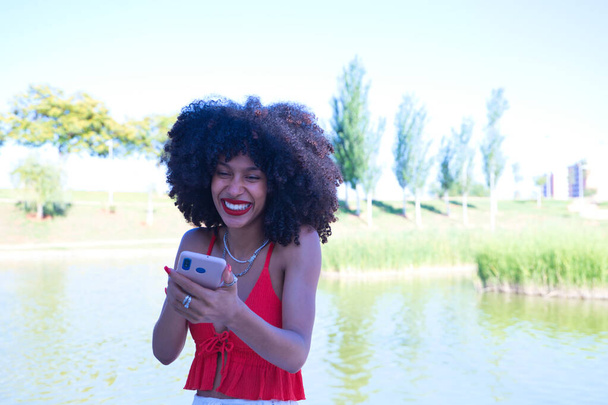 Bella donna afro-americana che parla in videochiamata è molto felice. La donna indossa un top rosso. Concetto di videochiamata. - Foto, immagini
