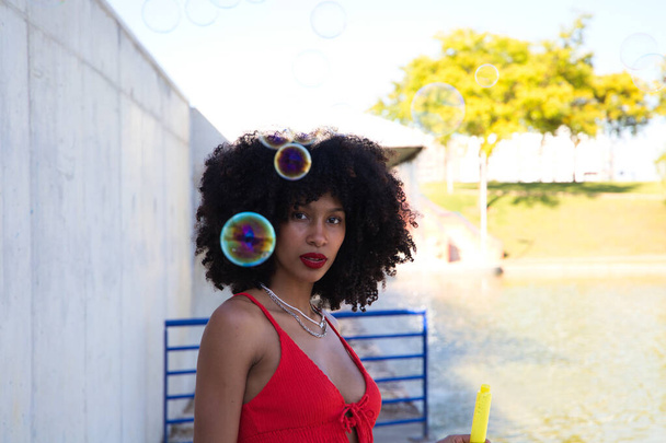 Krásná afro-americká žena si hraje s mýdlovými bublinami. Žena fouká bubliny a schovává se mezi mýdlové bubliny. Koncept štěstí - Fotografie, Obrázek