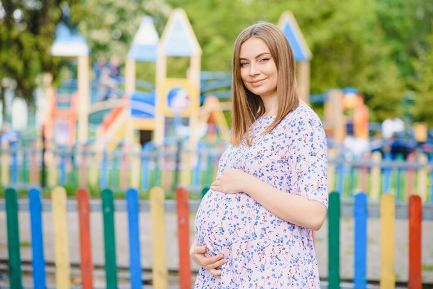 pregnant woman stands in the park near the playground where children play. - Foto, Imagem