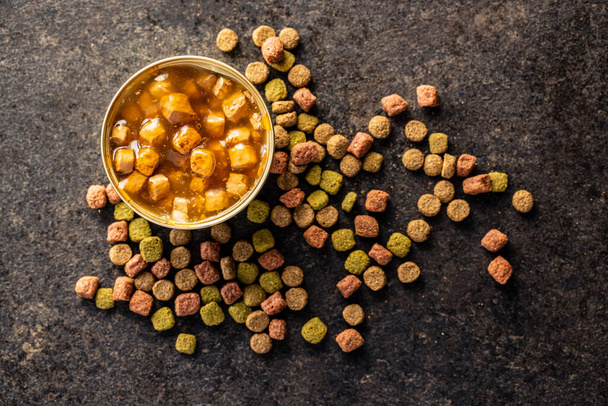 Canned pet food and dried kibble. Tasty food for dog or cat on black table. Top view. - Fotografie, Obrázek