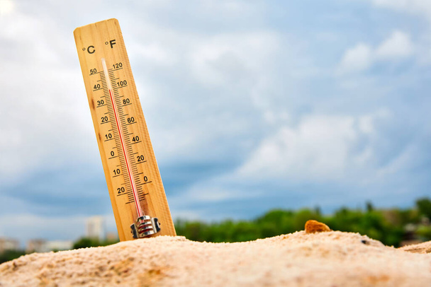 Termómetro meteorológico en la arena contra el cielo que muestra una alta temperatura ambiente - Foto, Imagen