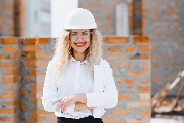 Construction engineer. Girl with construction documentation. A woman in a white hard hat against the roof of a building. Construction of a new house. - Foto, Bild
