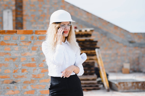 Absorbed in the work of a woman engineer working with a tablet on the background of the construction site. Portrait of a young architect, protective equipment. Selective focus. - Foto, Imagem