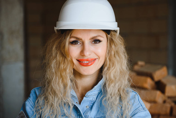 Construction engineer. Girl with construction documentation. A woman in a white hard hat against the roof of a building. Construction of a new house. - 写真・画像