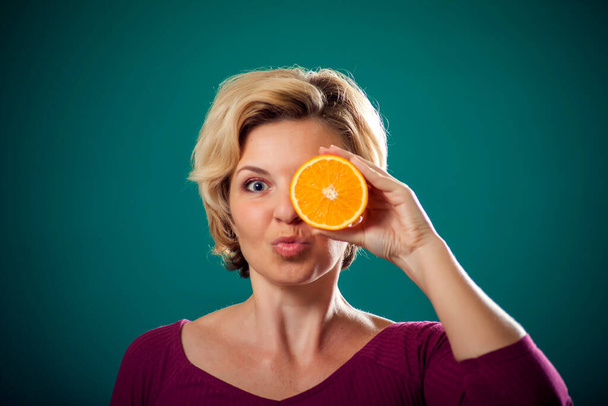 Ευτυχισμένη γυναίκα με κοντά ξανθά μαλλιά που κρατάει πορτοκαλί κοντά στο πρόσωπο. 'Ανθρωποι, τρόπος ζωής και υγεία - Φωτογραφία, εικόνα