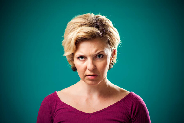 Femme en colère avec les cheveux blonds courts en face de fond vert. Concept des personnes et des émotions - Photo, image