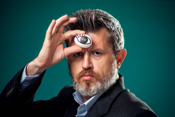 A portrait of bearded man in suit holding egg with drawing eye near forehead. Third eye concept - Photo, Image