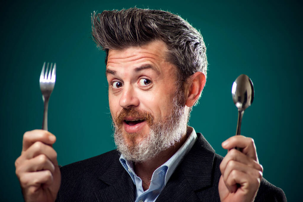Portrait d'un homme barbu affamé en costume tenant cuillère et fourchette.  - Photo, image