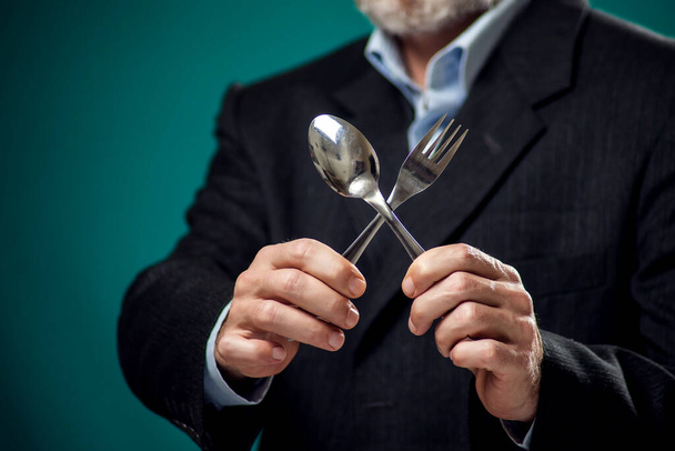 Ένα πορτραίτο ενός πεινασμένου γενειοφόρου άντρα με κοστούμι που κρατάει κουτάλι και πιρούνι.  - Φωτογραφία, εικόνα