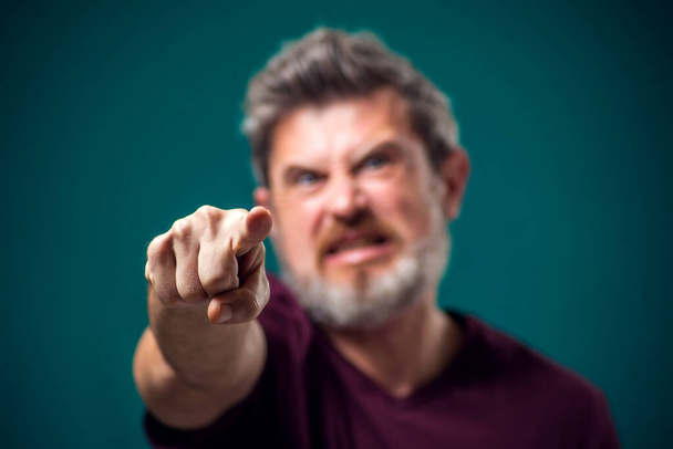 Um retrato de um homem barbudo furioso com uma t-shirt vermelha apontando o dedo para a câmara. Conceito de pessoas e emoções - Foto, Imagem