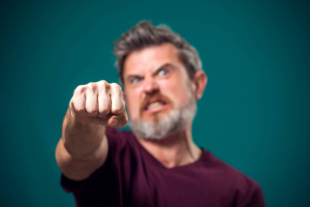 Een portret van een boze man met een baard in rood t-shirt met vuist op de camera. Mensen en emoties concept - Foto, afbeelding