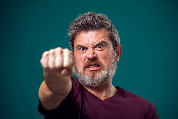 Un retrato de un hombre barbudo enojado con una camiseta roja mostrando el puño en la cámara. Concepto de personas y emociones - Foto, Imagen