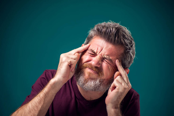 Портрет бородатого мужчины в красной футболке, размышляющего или страдающего головной болью. Человек, эмоции и концепция здоровья - Фото, изображение