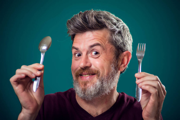 Portrait d'un homme barbu et affamé tenant cuillère et fourchette dans les mains. Les gens et le concept alimentaire - Photo, image