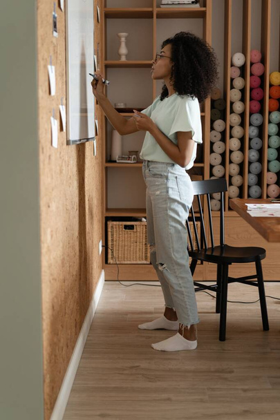 Focused young millennial african american woman in a casual clothes writes on the flip chart in the office - Foto, imagen
