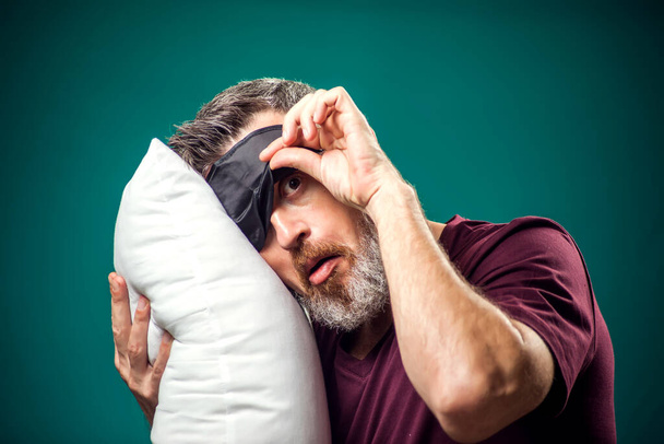 Homme en t-shirt rouge et masque de sommeil sur la tête tenant un oreiller blanc. Mode de vie et temps au lit concept - Photo, image