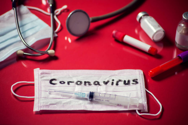 Maschera con parola-coronavirus, oggetti medicinali su sfondo rosso. Medine e concetto di assistenza sanitaria - Foto, immagini