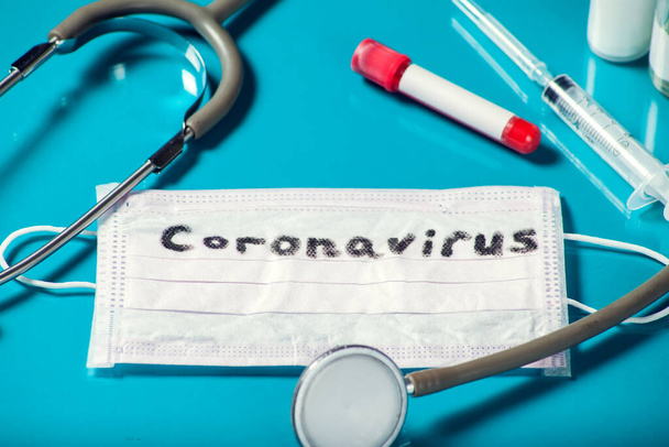 Masker met woord-coronavirus, medicijnen op blauwe achtergrond. Begrip "geneeskunde en gezondheidszorg" - Foto, afbeelding
