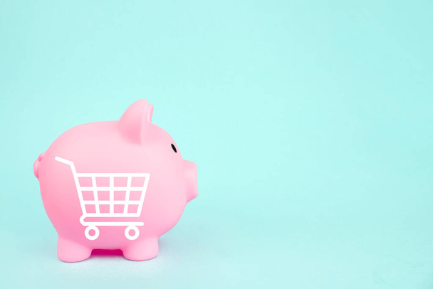 Pink piggy bank with mini shopping cart on blue background. Saving money for sales of the year, black friday concept - Photo, Image