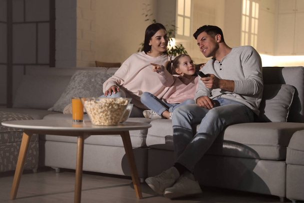 Family watching movie with popcorn on sofa at night - Fotó, kép