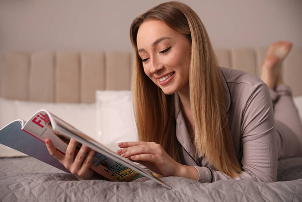 Happy woman reading magazine on bed indoors - Fotó, kép