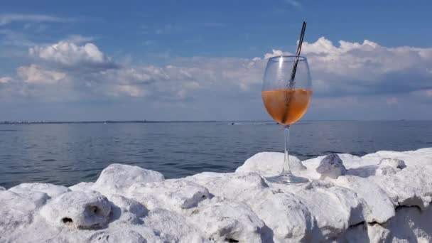 Statyczny widok kieliszek wina koktajlowego na białym kamiennym ogrodzeniu nad morzem z fal morskich tła - Materiał filmowy, wideo