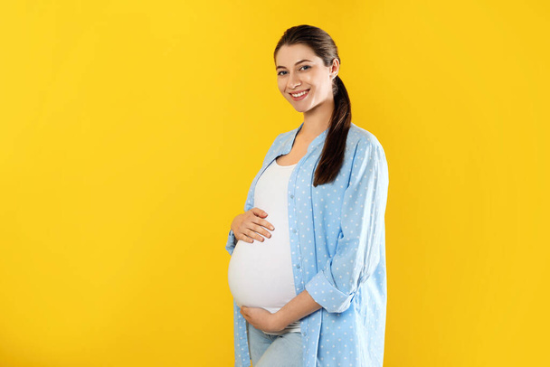 Happy young pregnant woman on yellow background, space for text - Valokuva, kuva