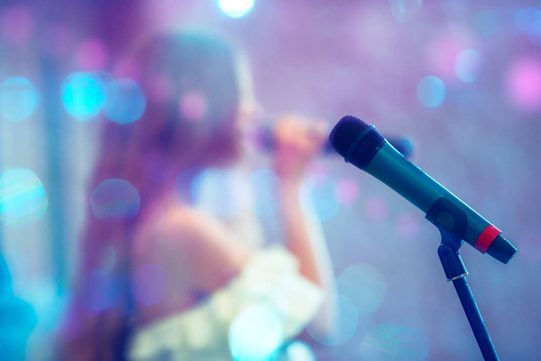 Microfone de palco contra o fundo de um cantor desfocado em manchas de bokeh azul. desempenho ou recital.Modern microfone e texto KARAOKE Noite no fundo azul - Foto, Imagem