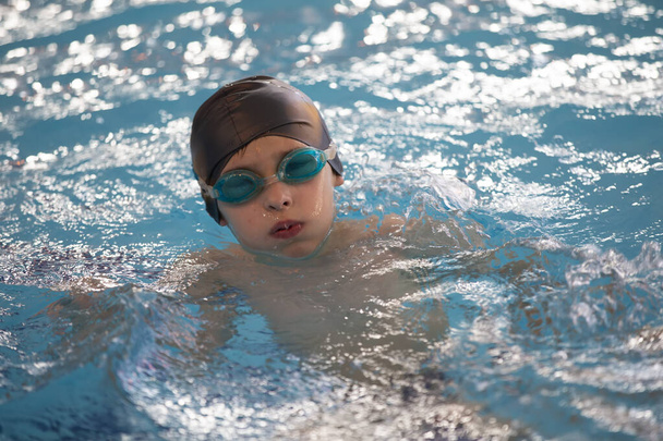 Úszósapkás fiú és úszószemüveg a medencében. A gyermek az uszodában van.. - Fotó, kép